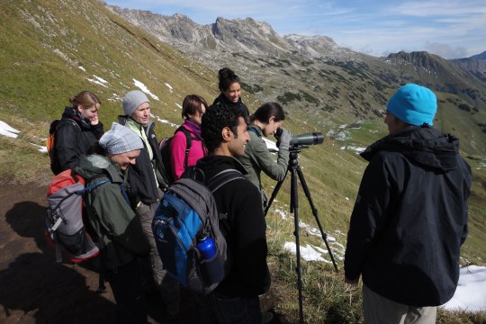 Exkursionsgruppe mit sieben Teilnehmern und dem Exkursionsleiter stehen auf einem Berg, ein Teilnehmer schaut durch ein Spektiv | © Henning Werth