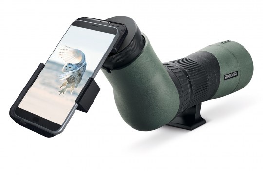 Smartphone eist mit einem Adapter an einem Swarovski-Spektiv befestigt, auf dem Display sieht man eine fliegende Schneeeule | © Swarovski Optik