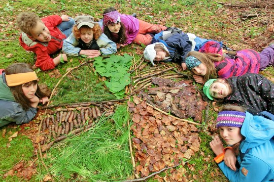 Acht Kinder liegen am Waldboden und haben einen runden Kreis aus Blättern und Ästen gebaut | © U. Jahn