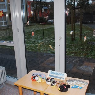 Große Fenster mit Tisch davor auf dem Plüschvögel liegen, außen sieht man die Futterstation | © LBV