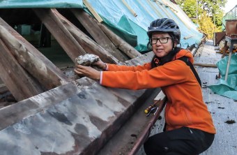 Susanne Rieck hat einen Helm auf und steht vor einem offenen Dach, scheinbar ein Nest in der Hand | © LBV